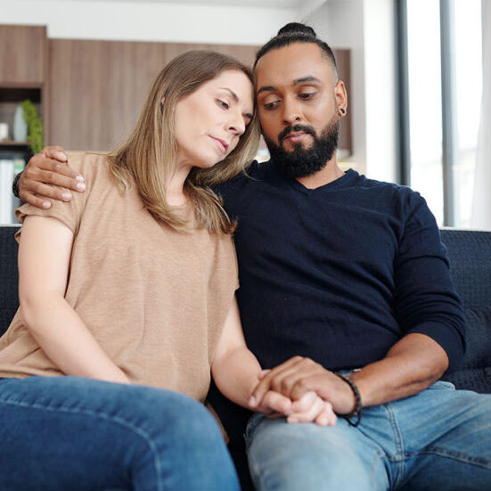 A man and woman sitting on the couch leaning against each other.