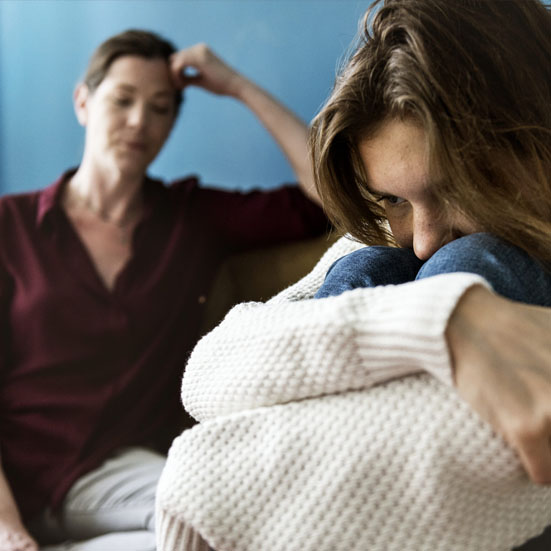 Young women in foreground with face in her knees, concerned older woman in background
